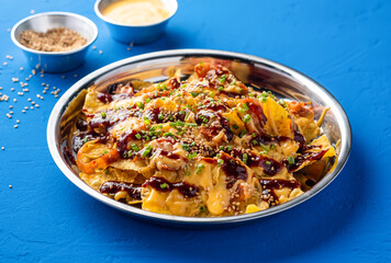 Loaded Fries Nachos with Kimchi, Chicken, Cheese, Sauce, Mayonnaise dip, sesame seeds and green onion served in plate isolated on blue background side view of fast food