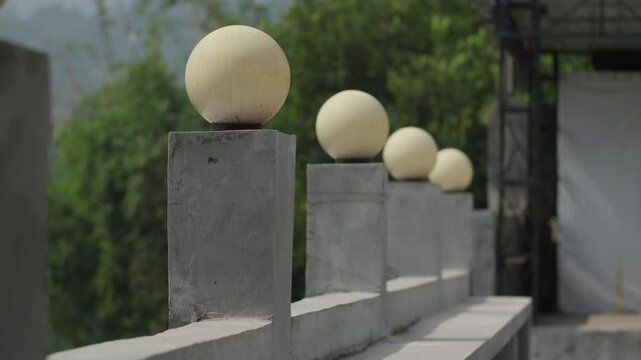 Concrete posts with round lights line up on an outdoor walkway in a green natural setting