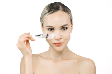 Fototapeta premium A beautiful woman applies face cream, ensuring perfect hydration for her healthy, fresh skin. This close-up emphasizes the importance of skincare against a white background.