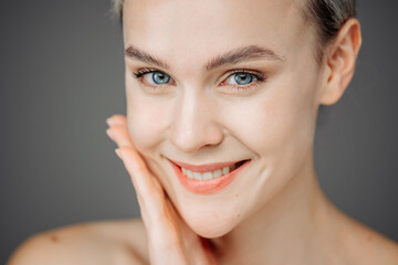 Obraz premium A young woman with radiant skin stands against a dark backdrop, showcasing her natural nude makeup. Her tender touch to her face emphasizes the importance of self-care and beauty.