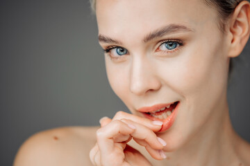 Obraz premium A young woman with radiant skin stands against a dark backdrop, showcasing her natural nude makeup. Her tender touch to her face emphasizes the importance of self-care and beauty.