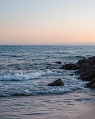 Calm ocean waves lapping at rocky shore under a pastel sunset sky.