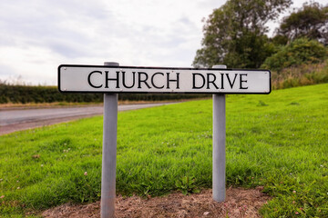White Church Drive road sign with green grass road, hedge and tree in background