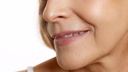 Naklejka premium Radiant close-up of woman's smile, slightly turned to side, emphasizing natural beauty and smooth skin against white studio background. Concept of beauty, wellness, cosmetology, anti-aging products.