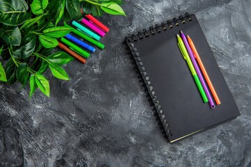 Colorful pens resting on a black notebook next to a small plant in a stylish flat lay design, showcasing modern desk essentials and workspace inspiration






