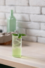 Green beverage served in tall glass, adorned with fresh basil leaf on light wooden surface in stylish setting