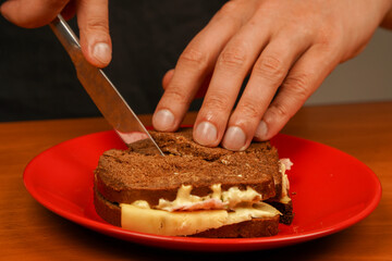 Cutting sandwich. Close-up of man eating sandwich. Close-up image of a male cooking and holding sandwich. Food. Tasty sandwich. Hands holding sandwich with ham, bacon, cheese, lettuce, tomatoes.