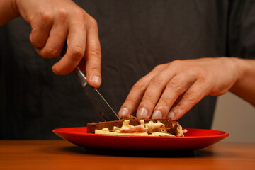 Close-up of man eating sandwich. Close-up image of a male cooking and holding sandwich. Food. Tasty sandwich. Hands holding sandwich with ham, bacon, cheese, lettuce, tomatoes. Cutting sandwich.