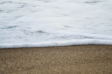 Closeup photo of beach sand and a small foamy wave coming in
