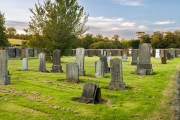 Old country cemetery with old gravestones surrounded by stone wall, green fields and trees at golden hour sunset © Tosh Lubek