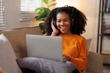 Happy millennial African American woman sitting on couch at home, get pleasant online message on laptop, chatting with friends via video call, talking in video chat, gestures with her hands.
