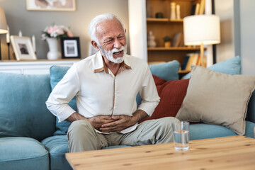 Stomachache concept. Sad mature man touching aching abdomen having acute stomach pain, sitting on...