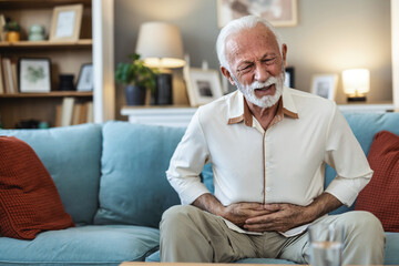 Stomachache concept. Sad mature man touching aching abdomen having acute stomach pain, sitting on...