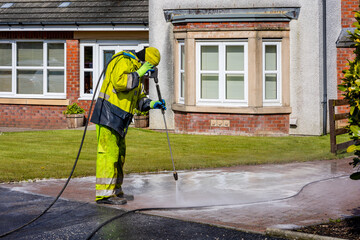 Worker in Yellow Protective Clothing Pressure Washing Monoblock Brick Paver Driveway