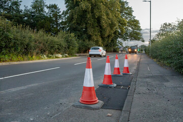 Line of orange and white plastic traffic cones at side of road, indicating resurfacing roadwork...