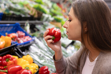 Woman smelling a fresh red bell pepper in a supermarket. Concept of choosing high-quality ingredients, freshness, and mindful food shopping for a healthy lifestyle