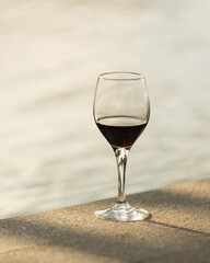 Glass of red wine basking in the rays of sunset beside the blurred background of the swimming pool.