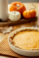 Delicious homemade pumpkin pie on orange napkin, perfect for autumn. Cozy, rustic setting with small pumpkins and a vase of flowers in the background