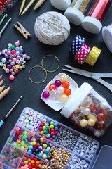 Colorful beads, coloring pencils, glitter, needles, string, hoop, tape and scissors on dark background. Various colorful craft supplies. Selective focus.