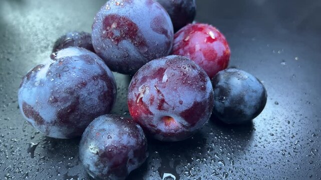 Water droplets clinging to freshly washed plums on black background