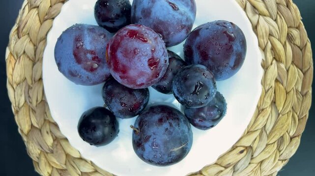 Wet, ripe plums and grapes slowly turn on a white plate