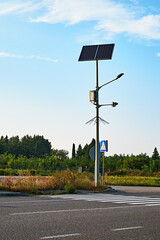 A solar-powered streetlight standing tall by a pedestrian crossing in a quiet, rural area.