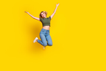 Obraz premium Full size photo of good mood positive girl dressed khaki crop top jeans jumping raising arms up isolated on yellow color background