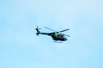 Helicopter is flying on isolated blue sky in mid-air background.