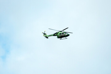 Helicopter is flying on isolated blue sky in mid-air background.