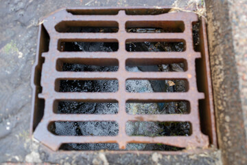 Rusty storm drain grate with rain water and debris flowing through with foamy bubbles