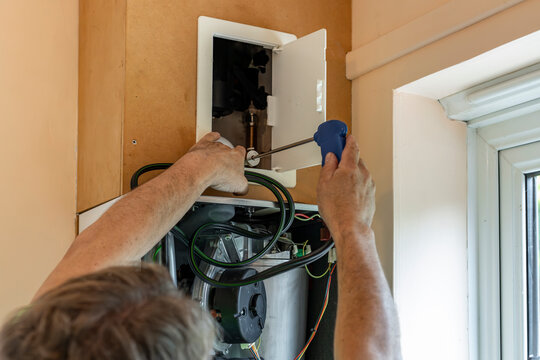 Gas service engineer attaching metal flue gas test probe to exit pipe above domestic boiler