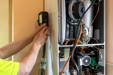 Gas service engineer holding digital flue gas analyser that is connected to domestic boiler by...