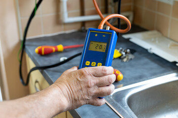 Gas service engineer holding digital differential manometer pressure meter connected to domestic...