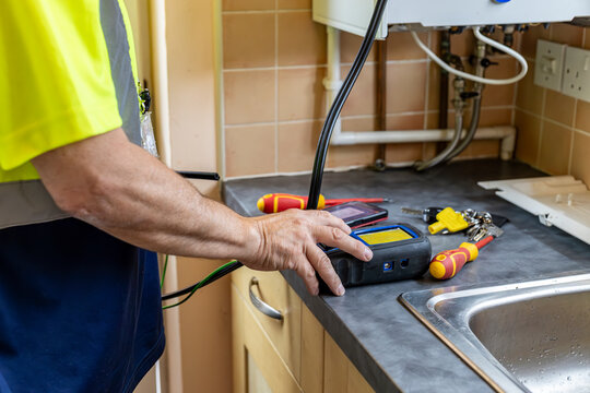 Gas service engineer operating digital flue gas analyser that is connected to domestic by black pipe