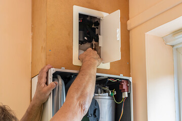 Gas service engineer technician reaching into boiler flue access panel on wall