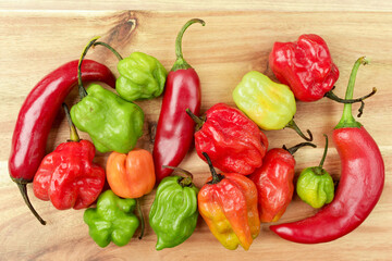Variety of colourful Chilli Peppers on wooden cutting board. Vivid colour close up photograph. Flat lay view.