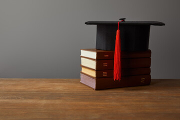 A graduation cap with a vibrant tassel sits atop a stack of vintage books, symbolizing the joy of...