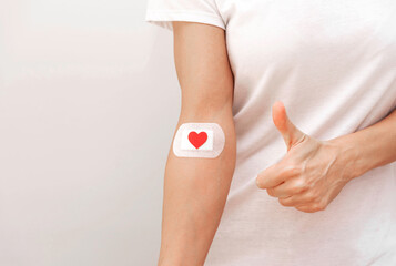 close up of blood donor arm with bandage and red heart with thumbs up gesture on grey background, blood donation concept with copy space
