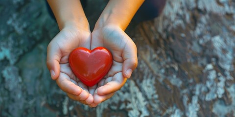 Fototapeta premium Child's hands holding a red heart symbol against a blurred outdoor background