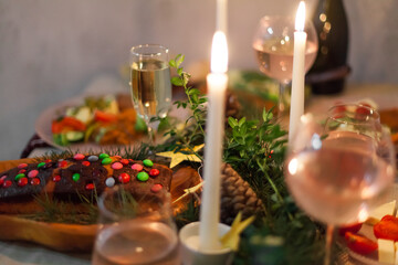 Christmas feast table with plates of food, glasses of wine and champagne, with festive decorations of pinecones, golden stars paper garland and long candles in evergreen foliage centerpieces
