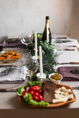 Christmas feast table with plates of food, glasses of wine and champagne, with festive decorations of pinecones, golden stars paper garland and long candles in evergreen foliage centerpieces