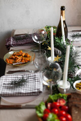 Christmas feast table with plates of food, glasses of wine and champagne, with festive decorations of pinecones, golden stars paper garland and long candles in evergreen foliage centerpieces
