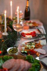 Christmas feast table with plates of food, glasses of wine and champagne, with festive decorations of pinecones, golden stars paper garland and long candles in evergreen foliage centerpieces