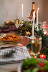 Christmas feast table with plates of food, glasses of wine and champagne, with festive decorations of pinecones, golden stars paper garland and long candles in evergreen foliage centerpieces