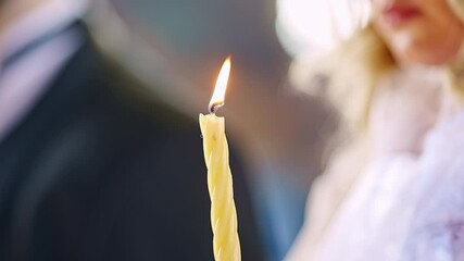 A burning church candle in the hands of the bride at the wedding in the church. Without faces. Christian traditions.