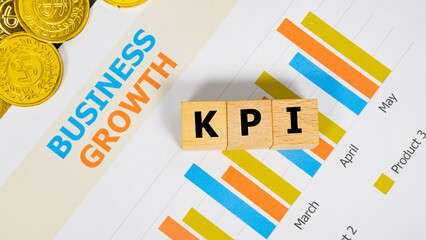 Obraz premium Three wooden blocks with the word KPI on a graph sheet with a pile of gold coins. Abbreviation for Key Performance Indicator, growth business and investment. Business and financial market concept.