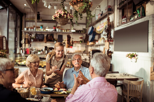 Smiling young waitress taking order from diverse senior people at a bistro
