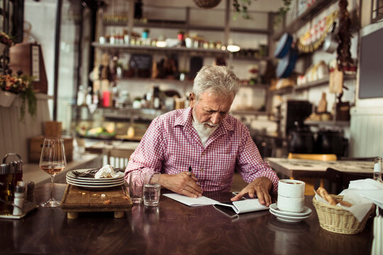 Senior bistro owner writing notes after busy day