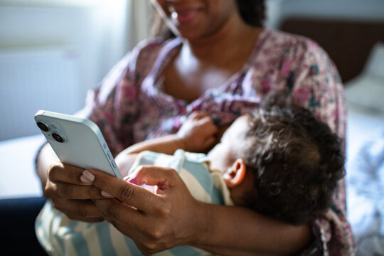 Mother breastfeeding while using smartphone at home