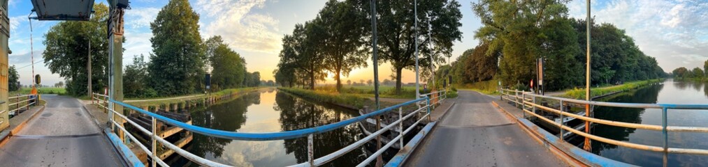 A beautifully picturesque view of a bridge that is surrounded by vibrant trees, reflecting sunset colors in the water
